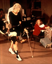 Figure 10.     A subject at the Massachusetts General Hospital with the pressure- instrumented endoprosthesis in her right hip joint and her motions and foot-floor forces concurrently measured by the MIT TRACK system. The electro-optical cameras detect the light-emitting diodes (LEDs) imbedded in arrays fastened to each body segment. Even the cane is force instrumented.